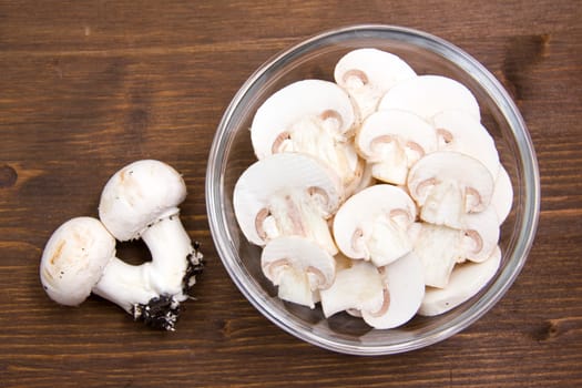 Sliced mushrooms in bowl on wooden table seen from above
