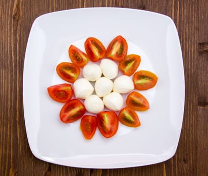 Plate with mozzarella and tomato on wooden table seen from above