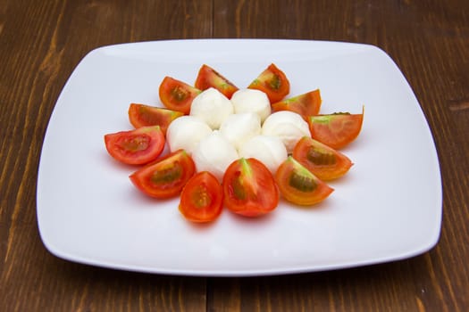 Plate with mozzarella and tomato on wooden table