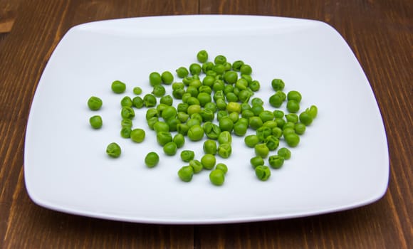 Plate with cooked green peas on wooden table