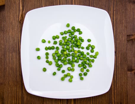 Plate with cooked green peas on wooden table seen from above