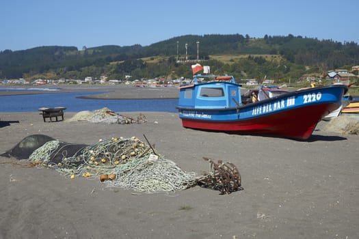 Colourfully painted wooden fishing boats drawn up on the on the beach in the small coastal town of Curanipe in Maule, Chile. The boats are pulled or pushed in and out of the sea using tractors.