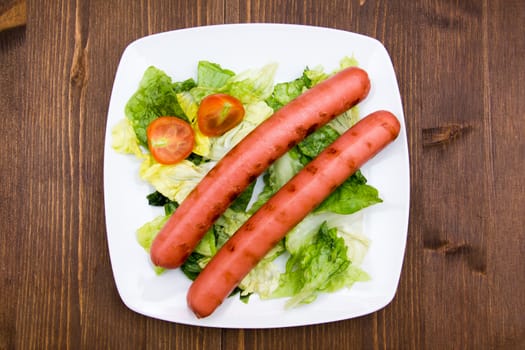 Sausages with salad on plate on wooden table seen from above