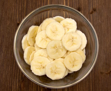 Banana slices on bowl on wooden table seen from above