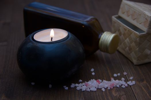 Candle with bath salts and oil on wooden table
