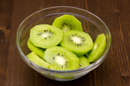 Slices of kiwi fruit on bowl on wooden table