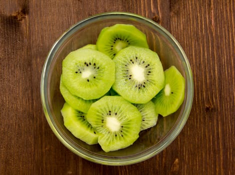 Slices of kiwi fruit on bowl on wooden table seen from above