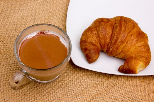 Croissant on plate and cappuccino in hessian placemat