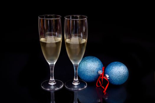 Flute with sparkling and christmas balls which are reflected on a black background