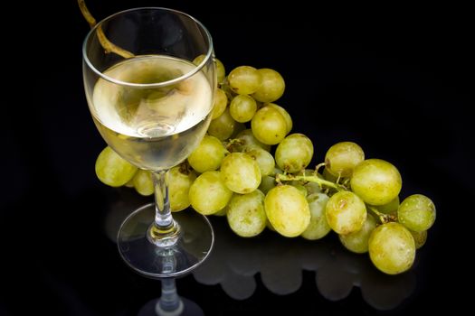 Wine glass with a bunch of grapes reflected on black background