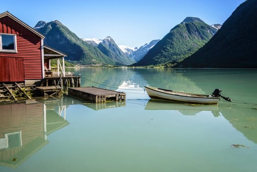 Reflection of a boat, a jetty, a red boathouse and mountains in the tranquil water of Fjærlandsfjord, part of the Sognefjord in the village of Fjærland or Mundal, Sogn og Fjordane, Fjord Norway.
