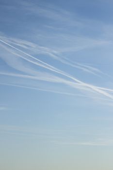 Blue sky with gray white clouds shot from airplane window in flight flying over the clouds on winter day with vapor trails.