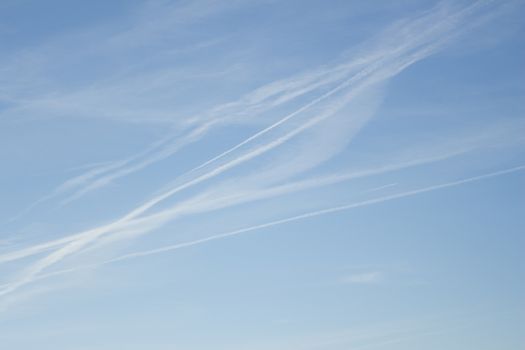 Blue sky with gray white clouds shot from airplane window in flight flying over the clouds on winter day with vapor trails.