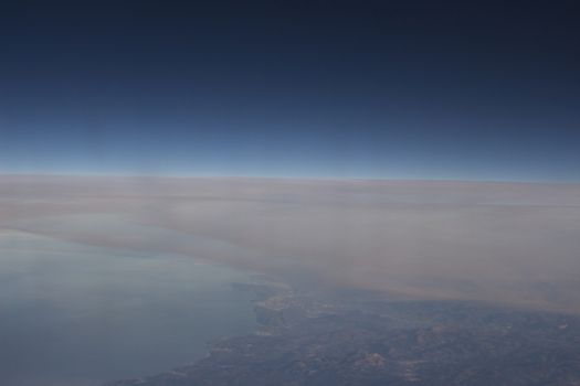 Blue sky with gray white clouds and ground shot from airplane window in flight flying over the clouds on winter day.