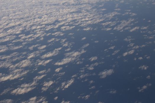 Blue sky with gray white clouds shot from airplane window in flight flying over the clouds on winter day.