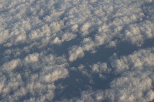 Blue sky with gray white clouds shot from airplane window in flight flying over the clouds on winter day.