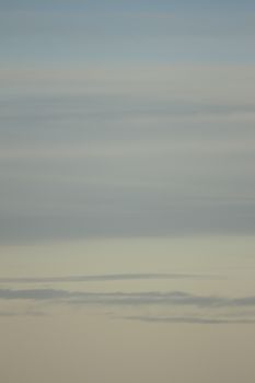 Blue sky with gray white clouds shot from airplane window in flight flying over the clouds on winter day.