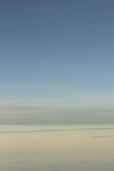 Blue sky with gray white clouds shot from airplane window in flight flying over the clouds on winter day.