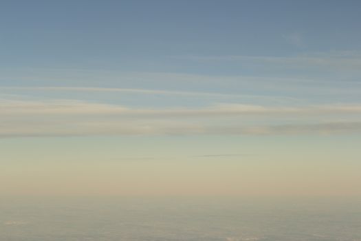 Blue sky with gray white clouds shot from airplane window in flight flying over the clouds on winter day.