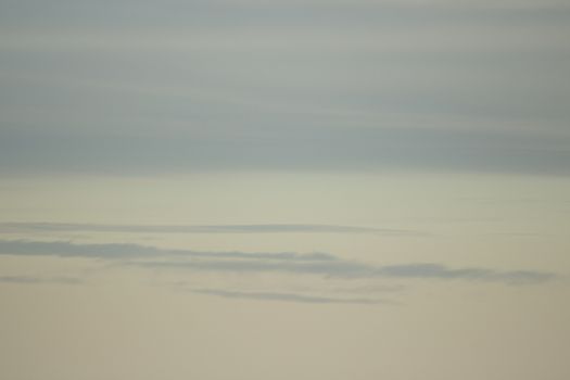 Blue sky with gray white clouds shot from airplane window in flight flying over the clouds on winter day.