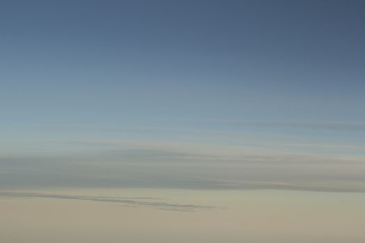 Blue sky with gray white clouds shot from airplane window in flight flying over the clouds on winter day.