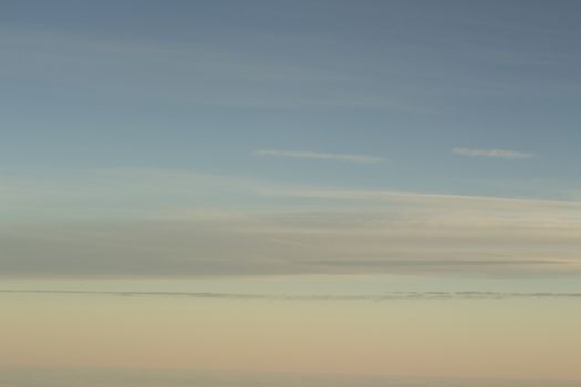 Sky with clouds in blue and pink purple sunset evening pastel colors photo shot from an airplane in flight flying above the cloud level.