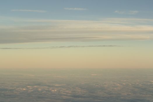 Sky with clouds in blue and pink purple sunset evening pastel colors photo shot from an airplane in flight flying above the cloud level.