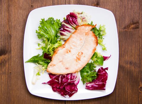 Chicken and salad on plate on wooden table seen from above