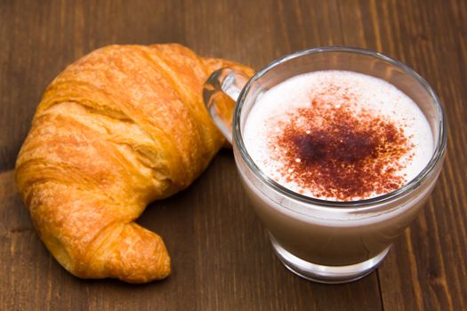 Cappuccino and croissant seen up close over wooden table