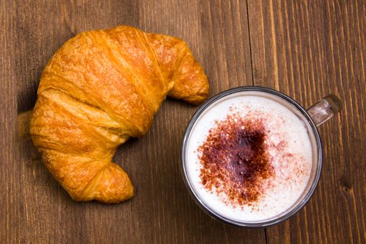 Cappuccino and croissant seen from above wooden table