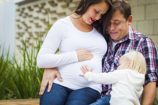 Adorable Baby Girl Puts Her Hand On Stomach of Mommy As Daddy Looks On.