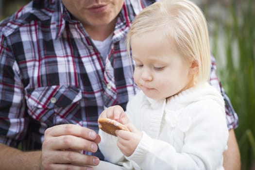 Adorable Little Girl Eating a Cookie with Daddy Outside.