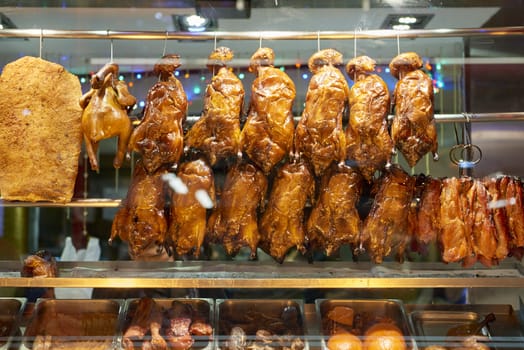 Detail of Chinese restaurant with traditional crispy ducks hanging on foggy display window in London's Chinatown at night.