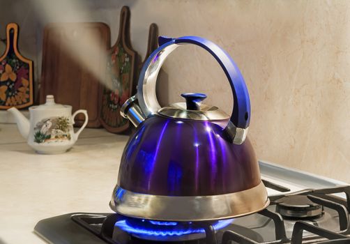 Blue kettle with a signal of boiling water and steam jet from the spout is on the burning gas stove