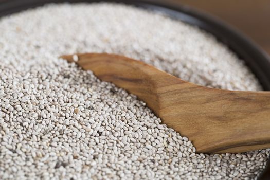 Healthy white chia seeds in bowl with wooden spoon.