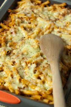 Baked ziti in a pan with a wooden spoon, ready to serve.