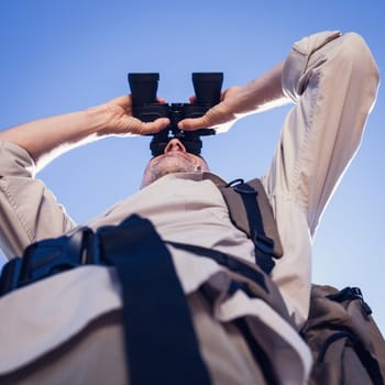 Hiker looking through binoculars on country trail on a sunny day