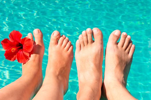 feet of a young couple by the pool with a red flower