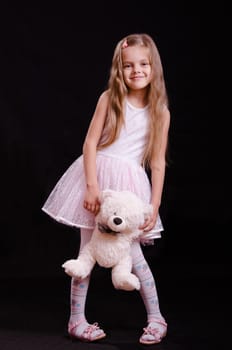 Portrait of a beautiful five year old girl with a teddy bear on a black background