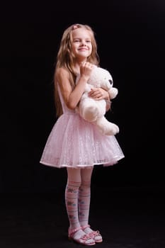 Portrait of a beautiful five year old girl with a teddy bear on a black background