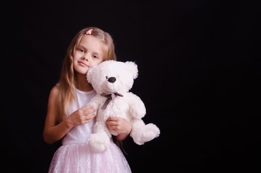 Portrait of a beautiful five year old girl with a teddy bear on a black background