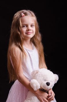 Portrait of a beautiful five year old girl with a teddy bear on a black background