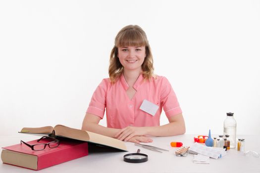 Pharmacist sitting at the table reading a thick handbook of medicines