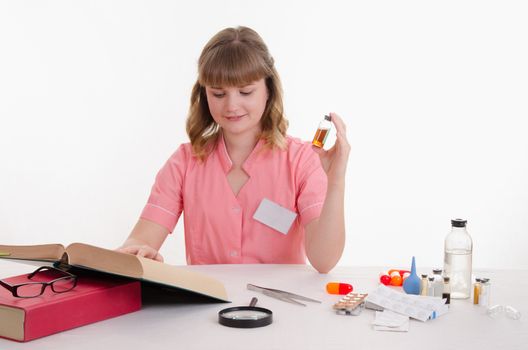 Pharmacist sitting at the table reading a thick handbook of medicines