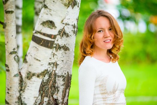 Russian red-haired girl in a park near a birch