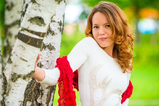 red-haired girl in a white dress near a birch