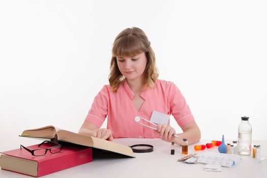Pharmacist sitting at the table reading a thick handbook of medicines