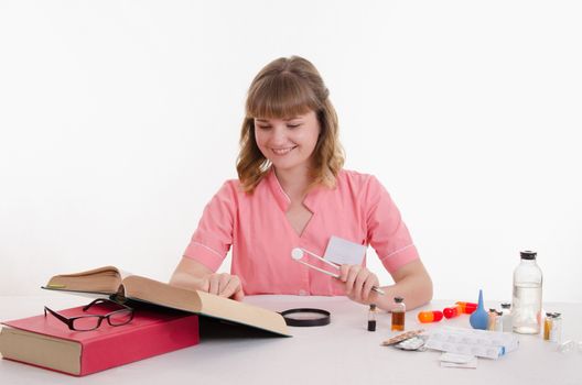 Pharmacist sitting at the table reading a thick handbook of medicines