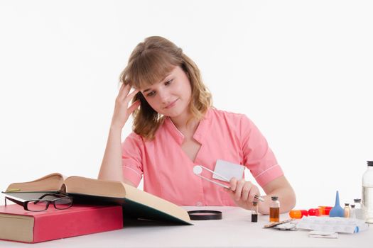 Pharmacist sitting at the table reading a thick handbook of medicines