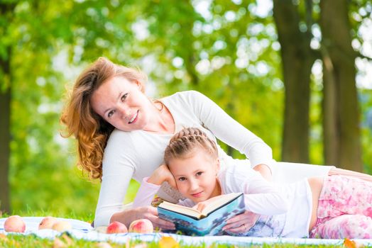 Mom and daughter reading a book lying in the park